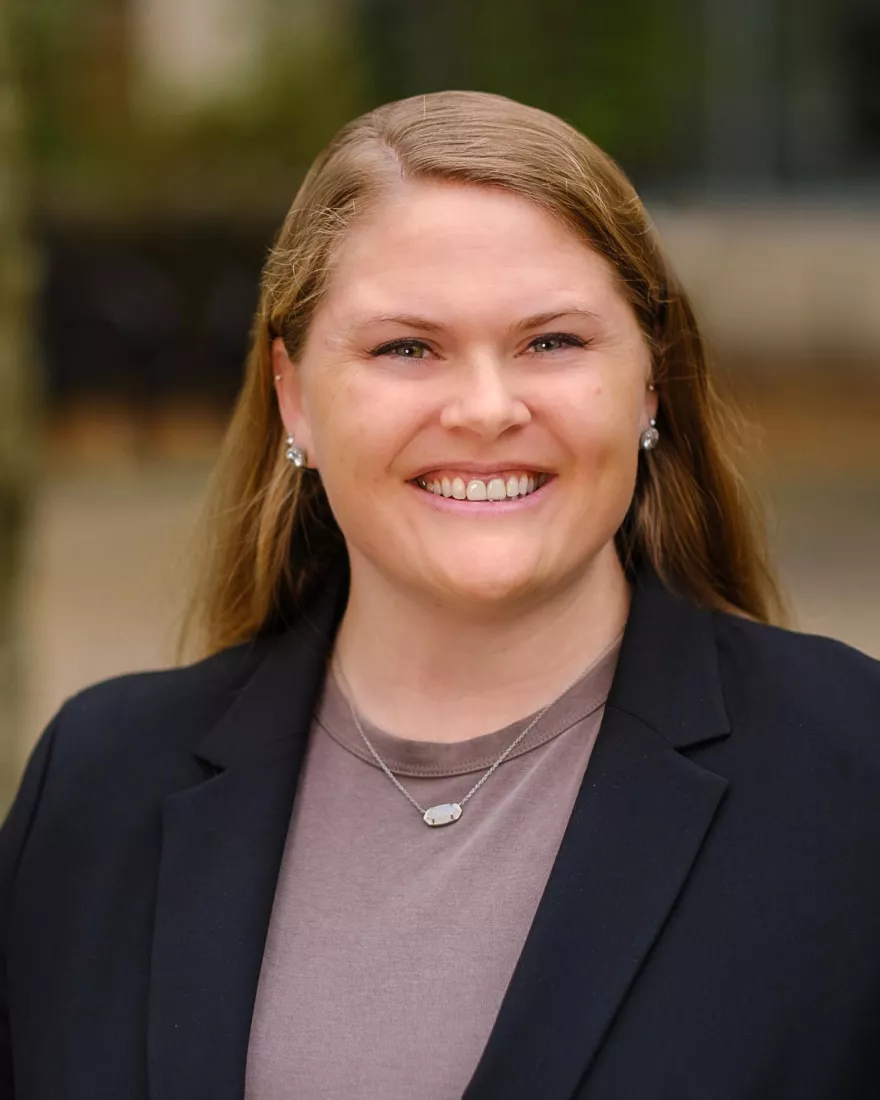 White woman with blonde hair wearing a brown shirt and a black blazer.