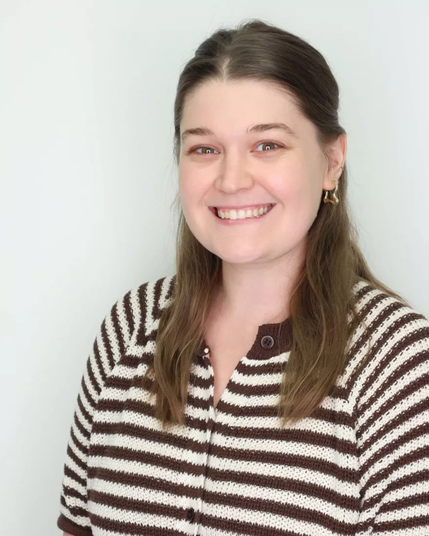 White woman with brown hair and a brown and white striped sweater. 