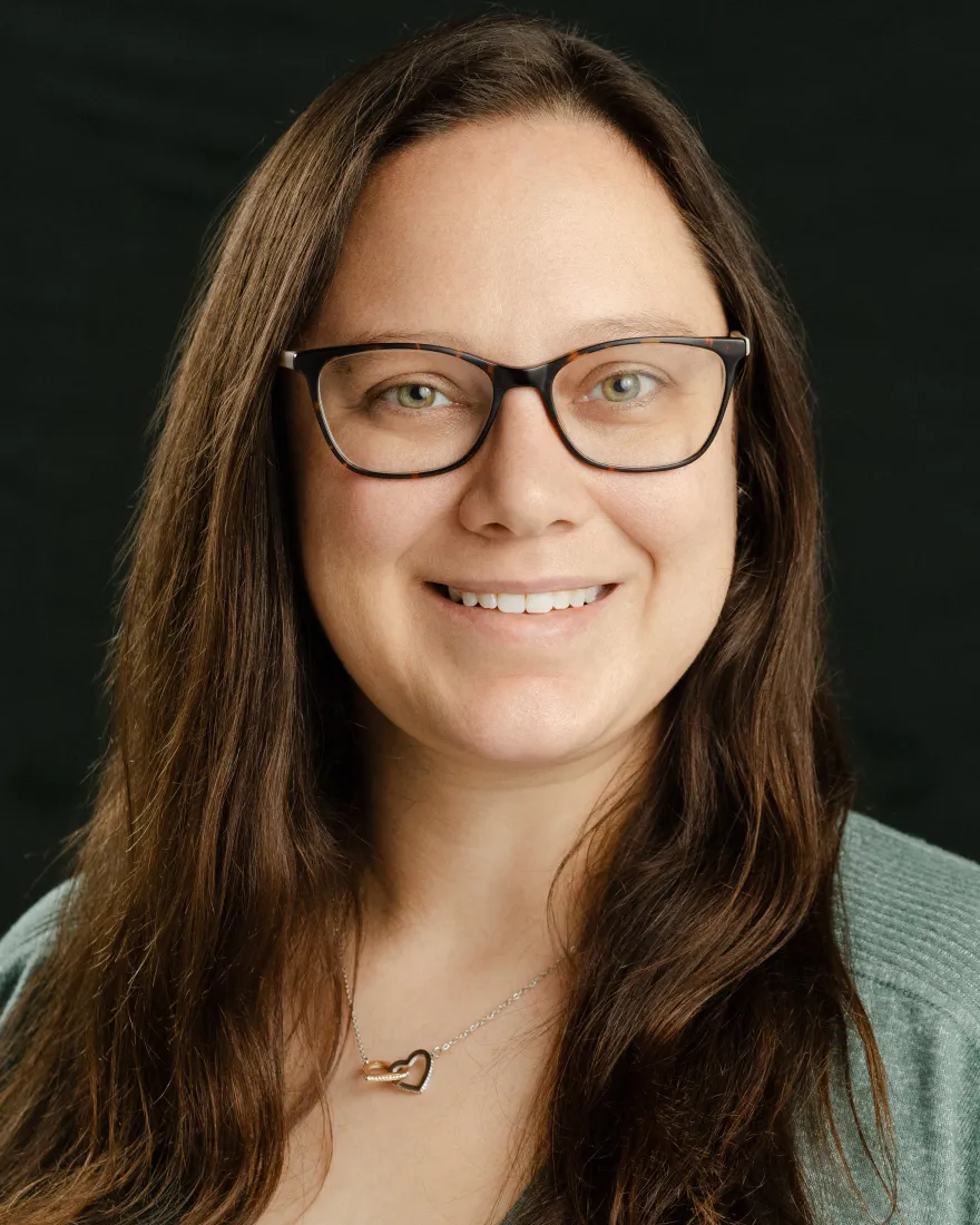 Smiling woman with glasses, green eyes, and long brown hair