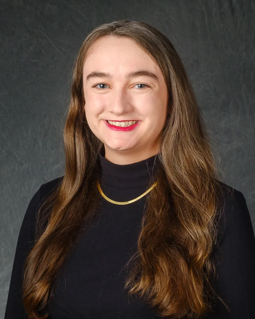 Photo of Alivia Stevens, smiling lady in a black shirt with a gold necklace.